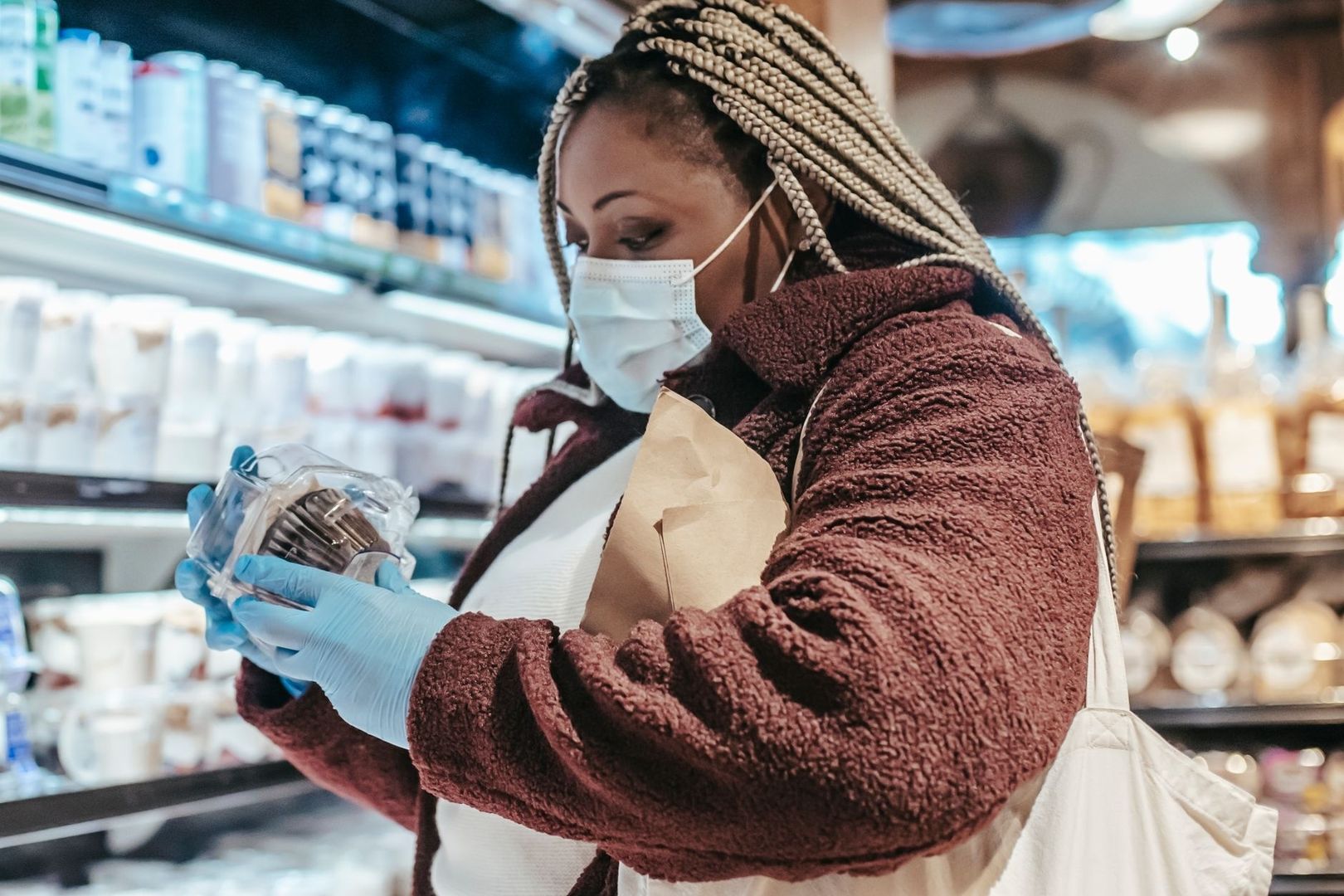 Gemaskerde vrouw bekijkt een verpakt product in een supermarkt