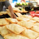 Marktkraam met verpakte voedingsmiddelen en een hand die een schaal aanwijst